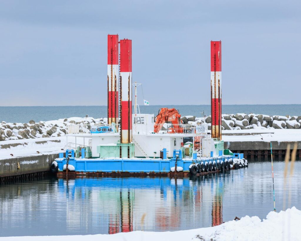 A dredging barge docked in the snowy harbor of Rumoi, Hokkaido, Japan, during winter.